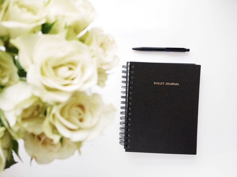 Czarny bullet journal i bukiet białych róż na biurku