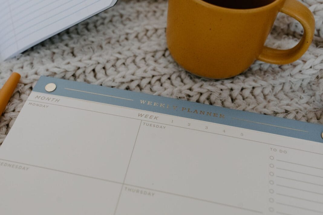 Tygodniowy planner, kubek kawy i dziergany koc na biurku Tygodniowy planner, kubek kawy i dziergany koc na biurku